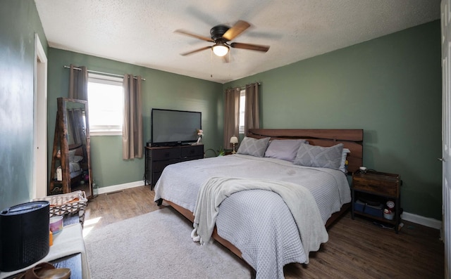 bedroom with multiple windows, wood finished floors, baseboards, and a textured ceiling