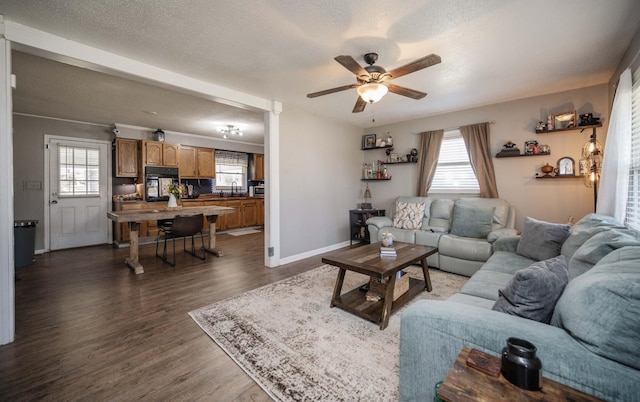 living area featuring a textured ceiling, a ceiling fan, dark wood-style floors, and a healthy amount of sunlight