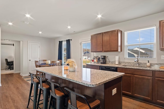 kitchen with a kitchen island, a kitchen bar, light stone counters, dark wood-style floors, and a sink