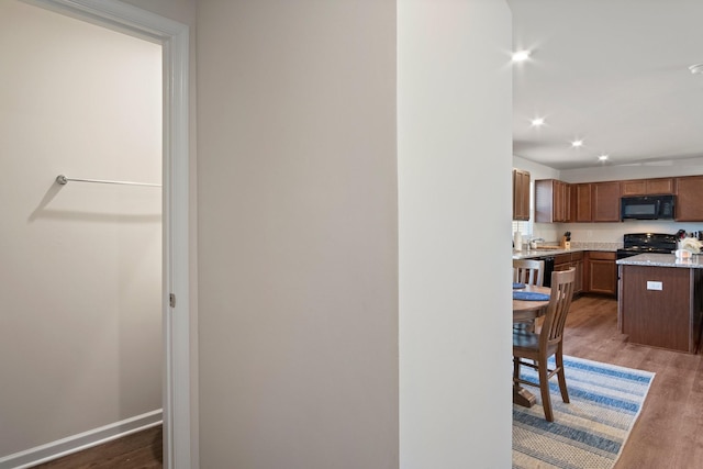 kitchen with a sink, baseboards, black appliances, and wood finished floors