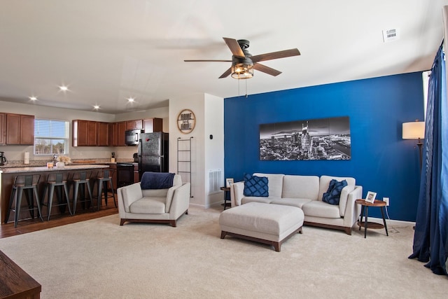 living room with baseboards, a ceiling fan, visible vents, and light carpet