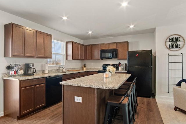 kitchen featuring wood finished floors, black appliances, a breakfast bar, and a center island