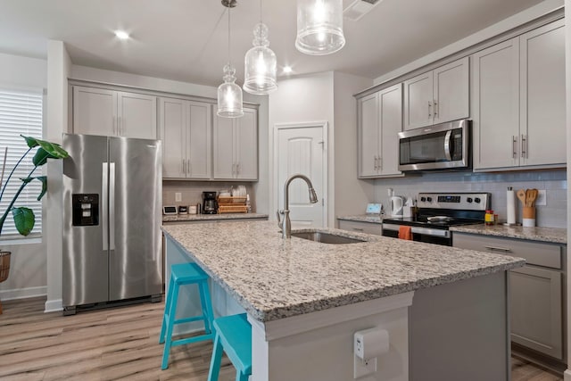 kitchen featuring appliances with stainless steel finishes, an island with sink, gray cabinetry, and a sink