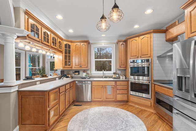 kitchen featuring decorative columns, a sink, stainless steel appliances, glass insert cabinets, and decorative light fixtures