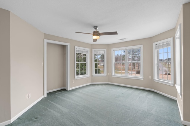 carpeted spare room with visible vents, a ceiling fan, and baseboards