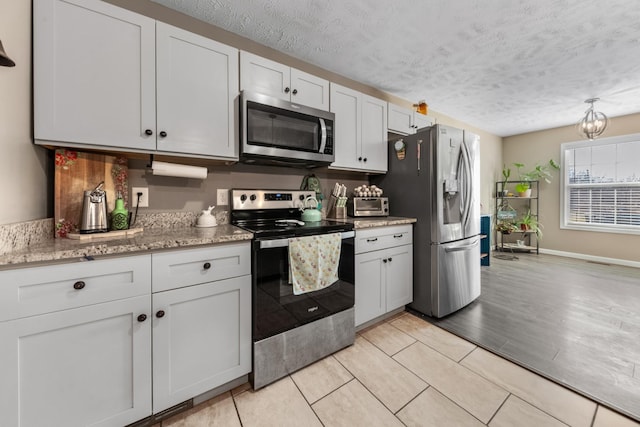 kitchen featuring appliances with stainless steel finishes, a textured ceiling, baseboards, and light stone countertops