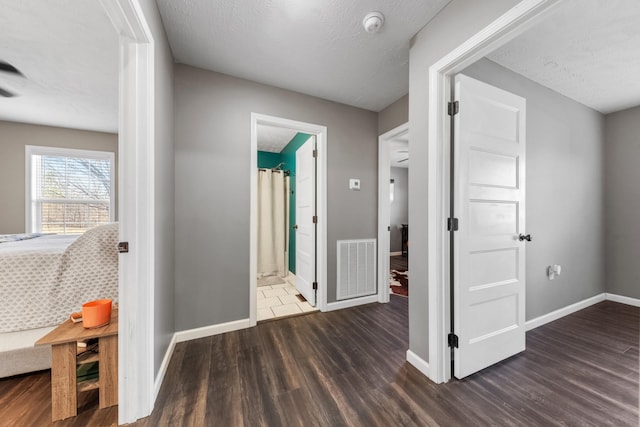 corridor with visible vents, a textured ceiling, baseboards, and wood finished floors