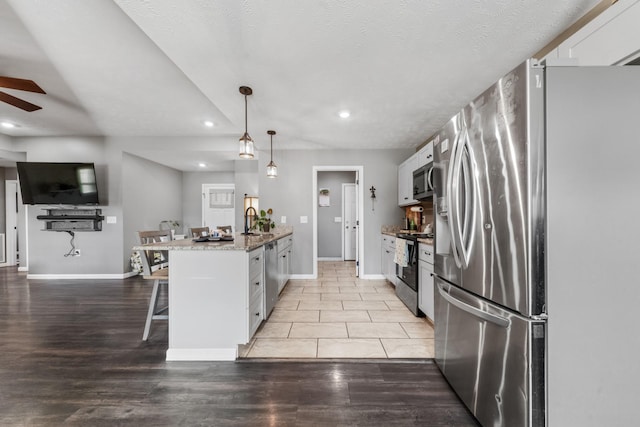 kitchen with a ceiling fan, white cabinetry, a peninsula, appliances with stainless steel finishes, and a kitchen bar