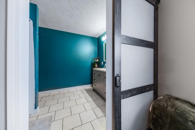 bathroom with vanity, baseboards, tile patterned flooring, and a textured ceiling