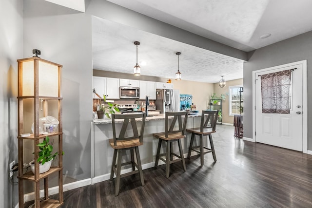 kitchen with dark wood-type flooring, a kitchen breakfast bar, white cabinetry, stainless steel appliances, and baseboards