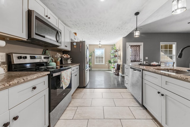 kitchen featuring light stone counters, light tile patterned flooring, a sink, appliances with stainless steel finishes, and a textured ceiling