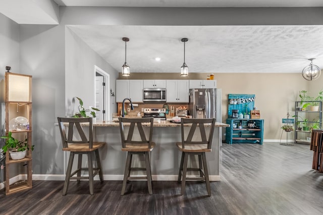 kitchen featuring baseboards, dark wood finished floors, a kitchen bar, light stone counters, and stainless steel appliances