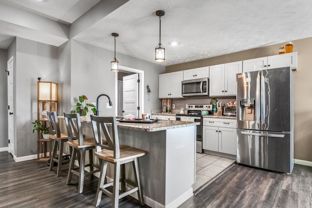 kitchen featuring baseboards, light stone countertops, appliances with stainless steel finishes, a kitchen breakfast bar, and wood finished floors