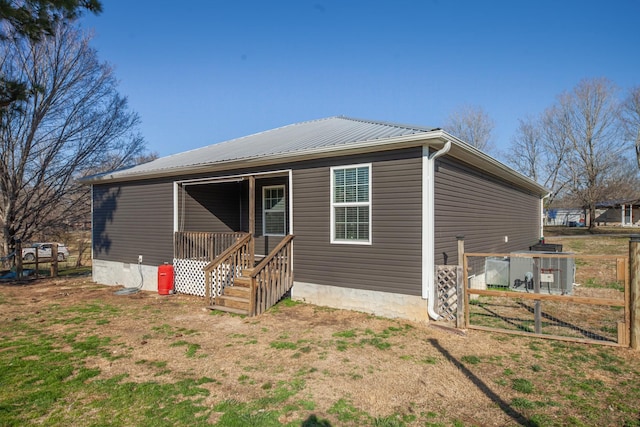 rear view of house featuring covered porch, metal roof, and fence