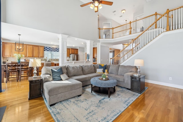 living area with a towering ceiling, stairway, light wood finished floors, baseboards, and ceiling fan