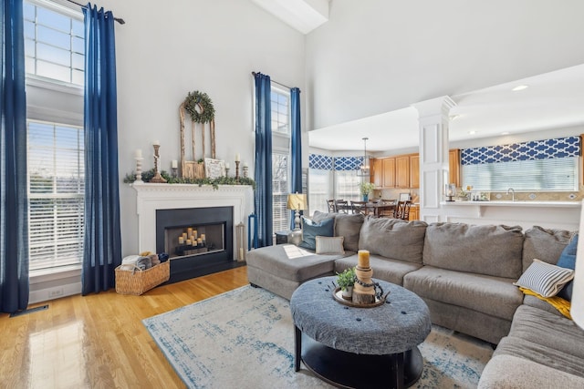 living room with ornate columns, a fireplace with flush hearth, a high ceiling, and light wood finished floors