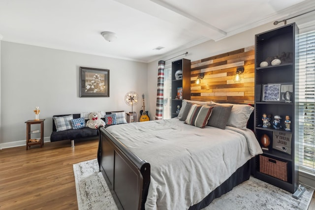 bedroom featuring wood finished floors, visible vents, baseboards, ornamental molding, and beamed ceiling