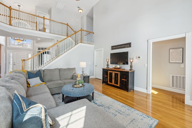 living area with visible vents, baseboards, stairway, a high ceiling, and wood finished floors