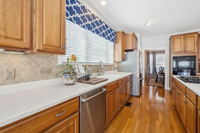 kitchen with light wood finished floors, backsplash, brown cabinetry, stainless steel appliances, and a sink