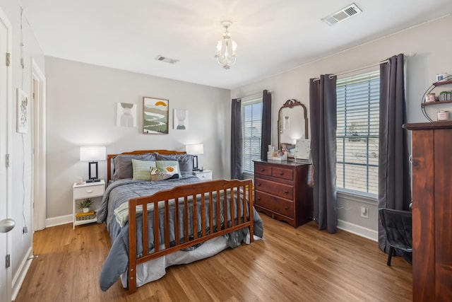 bedroom featuring visible vents, baseboards, a notable chandelier, and wood finished floors