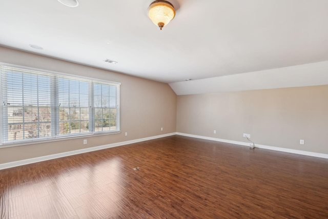 empty room with dark wood-type flooring, baseboards, visible vents, and vaulted ceiling