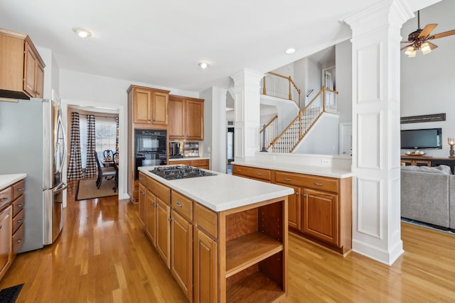 kitchen featuring appliances with stainless steel finishes, a kitchen island, light wood-style floors, and ornate columns