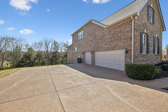 view of property exterior with a garage, brick siding, roof with shingles, and driveway