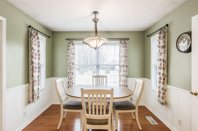 dining space featuring visible vents, a textured ceiling, baseboards, and wood finished floors