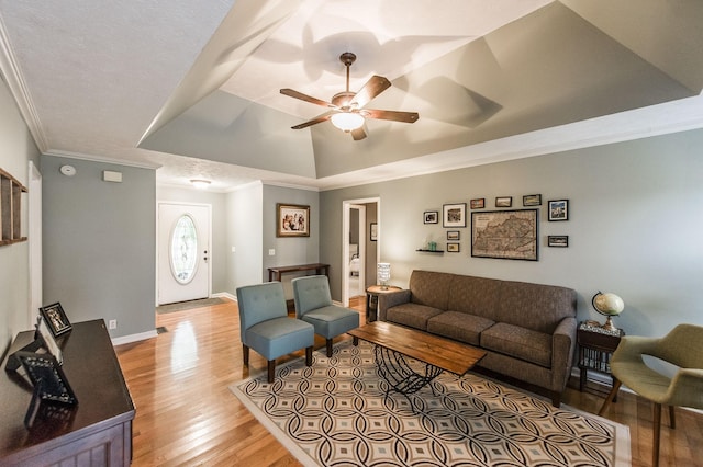 living area featuring a ceiling fan, a tray ceiling, light wood-style floors, crown molding, and baseboards