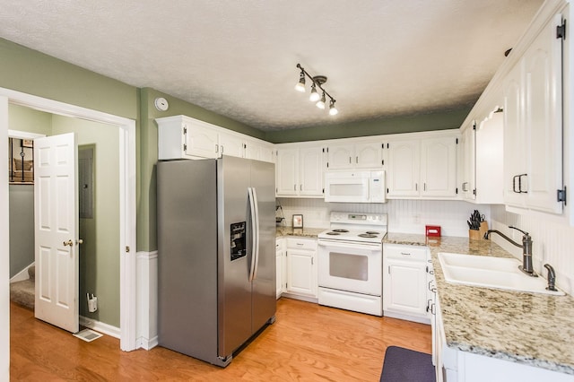 kitchen with white appliances, light stone countertops, a sink, light wood-style floors, and white cabinetry