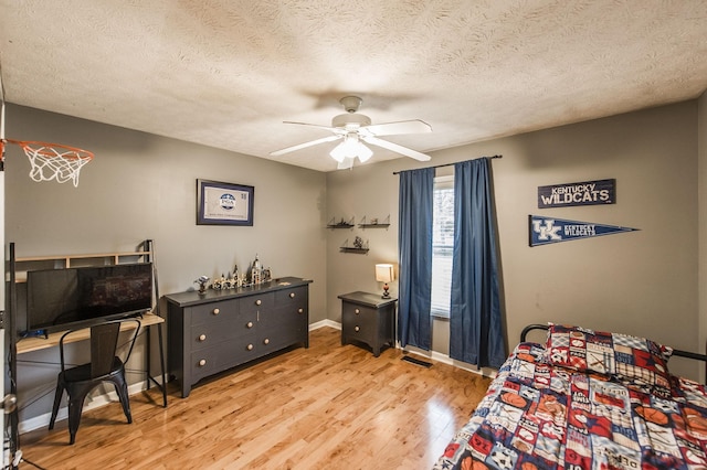 bedroom featuring a ceiling fan, visible vents, wood finished floors, baseboards, and a textured ceiling