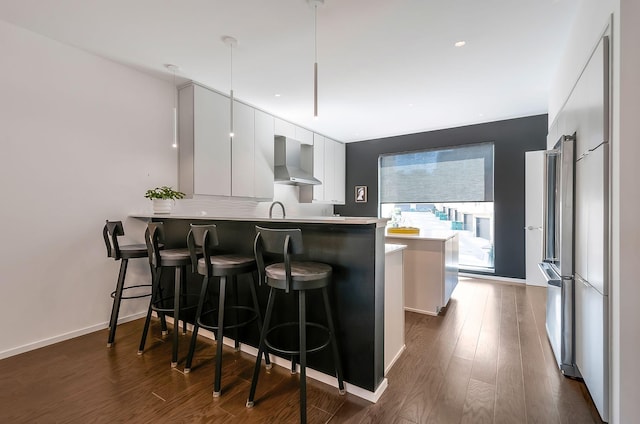 kitchen featuring a peninsula, white cabinetry, a kitchen breakfast bar, wall chimney exhaust hood, and modern cabinets