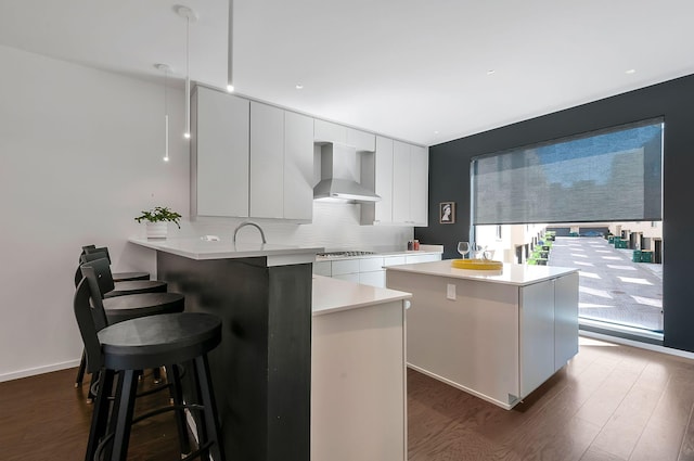 kitchen featuring wall chimney range hood, dark wood finished floors, a kitchen bar, light countertops, and modern cabinets