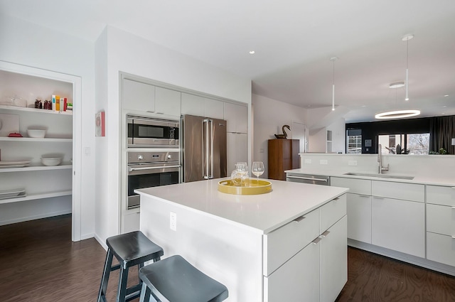 kitchen with a sink, a kitchen island, dark wood finished floors, stainless steel appliances, and light countertops