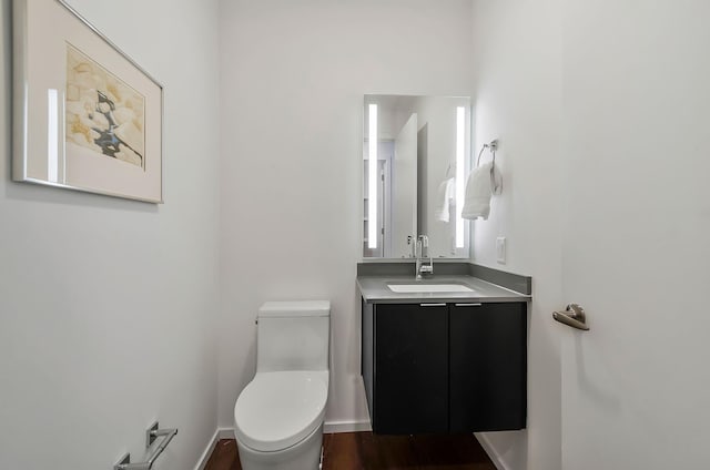 bathroom featuring baseboards, toilet, wood finished floors, and vanity