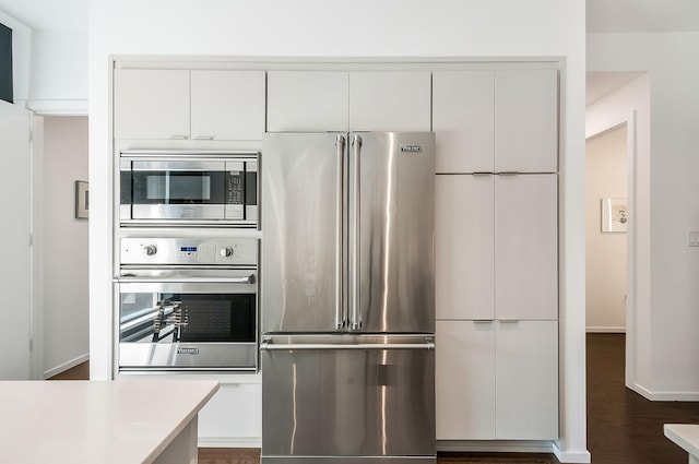 kitchen featuring dark wood finished floors, light countertops, stainless steel appliances, white cabinetry, and modern cabinets