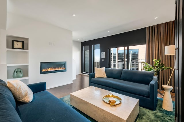 living area featuring a glass covered fireplace, recessed lighting, built in features, and dark wood-style flooring