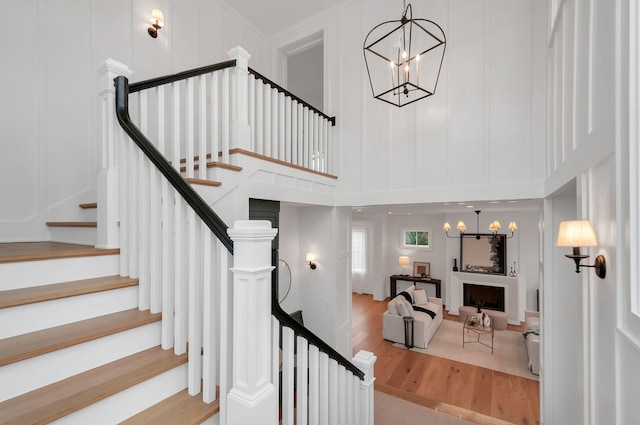 stairway with wood finished floors, an inviting chandelier, a fireplace, a towering ceiling, and a decorative wall