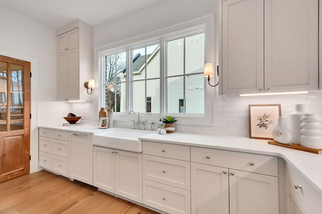 kitchen featuring a sink, light wood-style floors, white cabinets, light countertops, and decorative backsplash