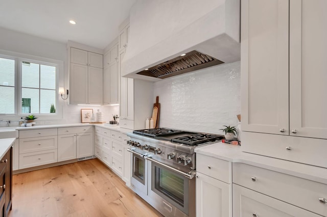 kitchen featuring backsplash, double oven range, light countertops, light wood-type flooring, and custom range hood