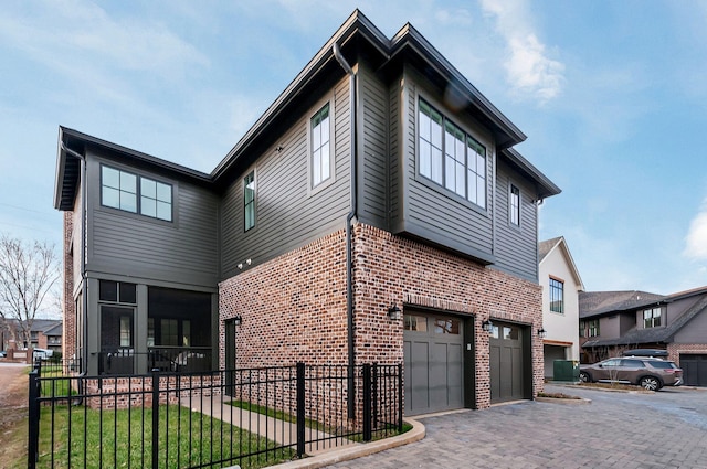 view of side of property featuring an attached garage, fence, brick siding, and driveway