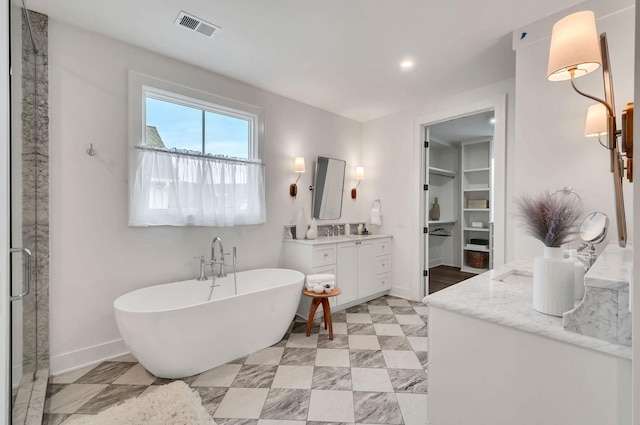 bathroom with a spacious closet, visible vents, baseboards, a soaking tub, and vanity