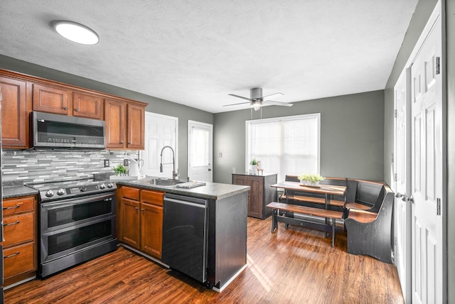 kitchen with a ceiling fan, a peninsula, dark wood-style flooring, a sink, and appliances with stainless steel finishes