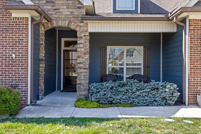 entrance to property with brick siding, covered porch, and roof with shingles