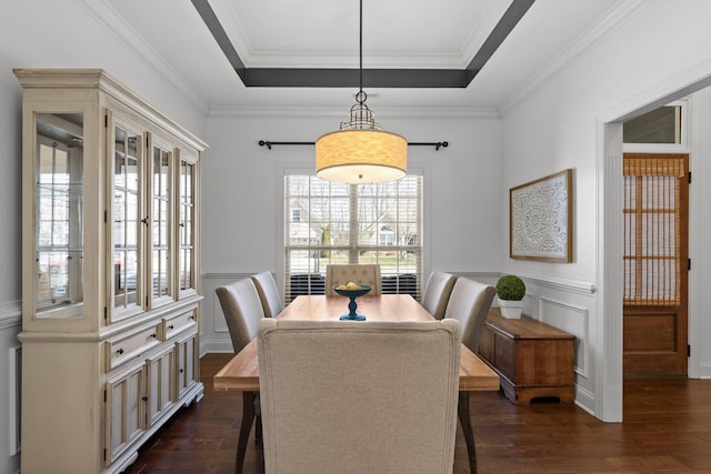 dining room featuring a raised ceiling, crown molding, a decorative wall, and dark wood-style floors