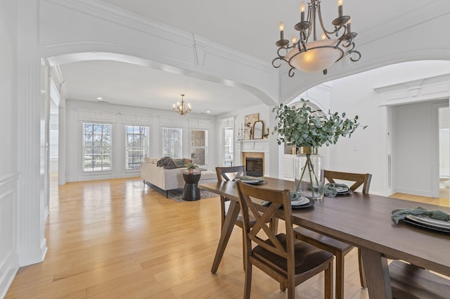 dining space with a notable chandelier, a fireplace, light wood-style floors, and arched walkways