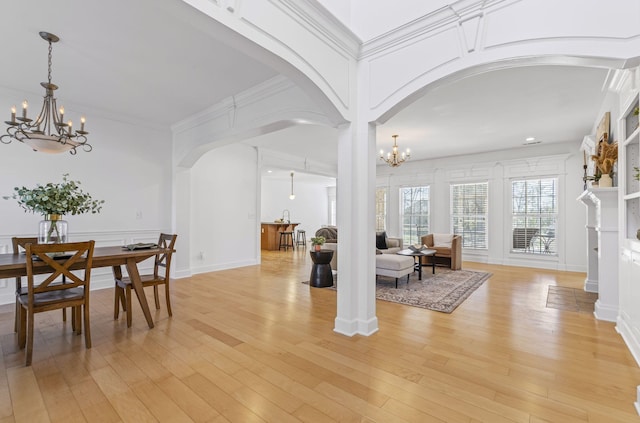 dining area with decorative columns, arched walkways, ornamental molding, a notable chandelier, and light wood-type flooring