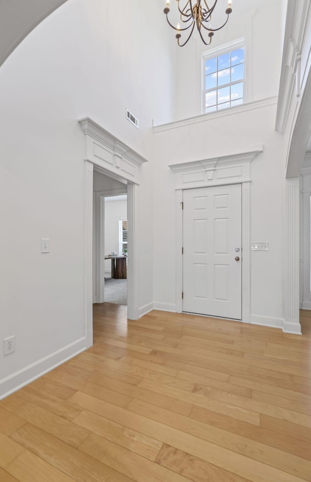 entrance foyer featuring visible vents, a high ceiling, light wood-style flooring, arched walkways, and a notable chandelier