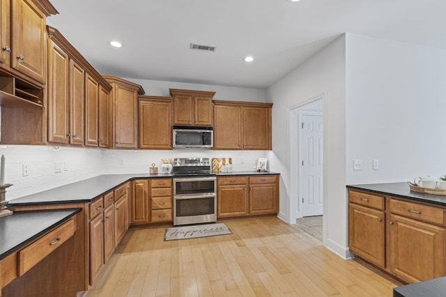 kitchen with dark countertops, brown cabinetry, stainless steel appliances, and light wood-type flooring