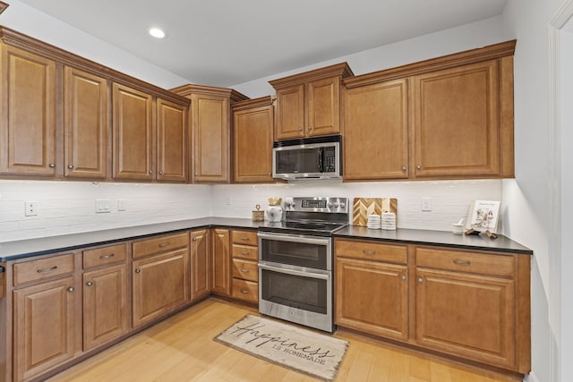 kitchen with dark countertops, light wood-style flooring, tasteful backsplash, and stainless steel appliances